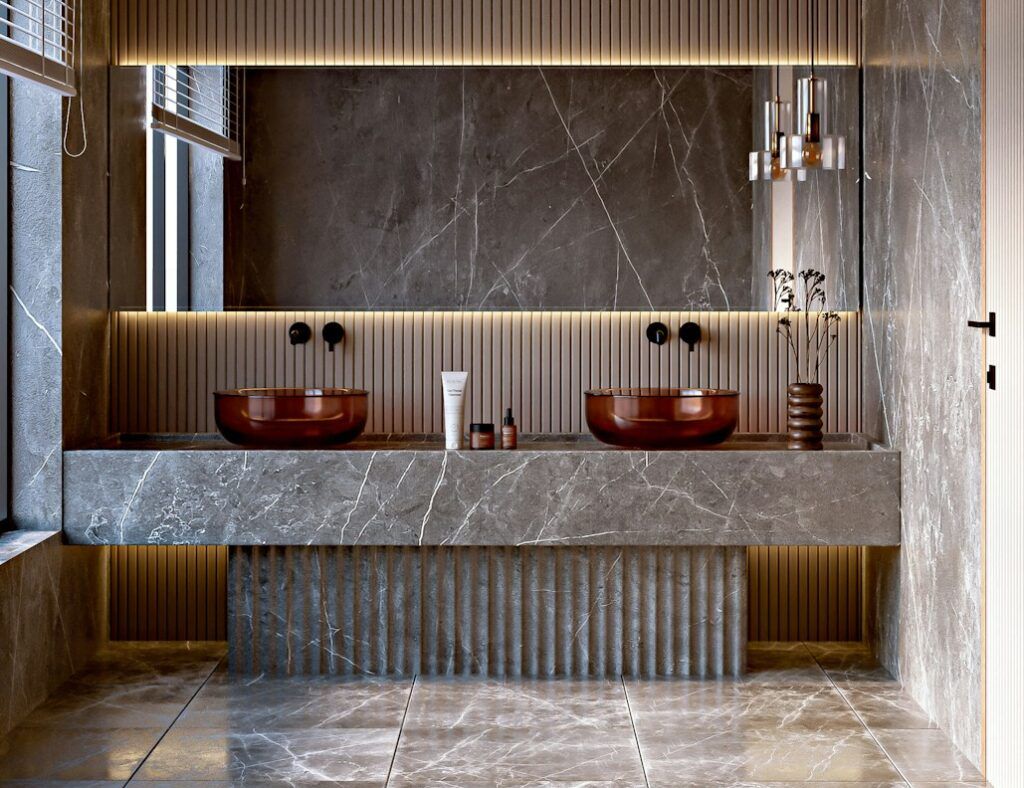 Modern bathroom with gray marble walls and floors showcasing expert flooring selection, two brown vessel sinks on a marble vanity, a large rectangular mirror with warm backlighting, vertical slatted wall accents, pendant lights, and a window with horizontal blinds on the left.