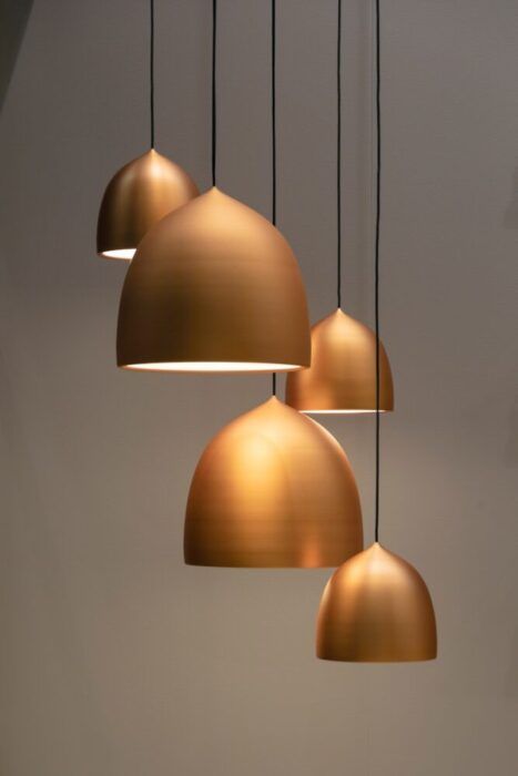 Four modern pendant lights with metallic gold dome-shaped shades hang at varying heights against a plain, light-colored wall. A Lighting Consultant in Weehawken can help you achieve this cozy and elegant look, perfect for any contemporary space.