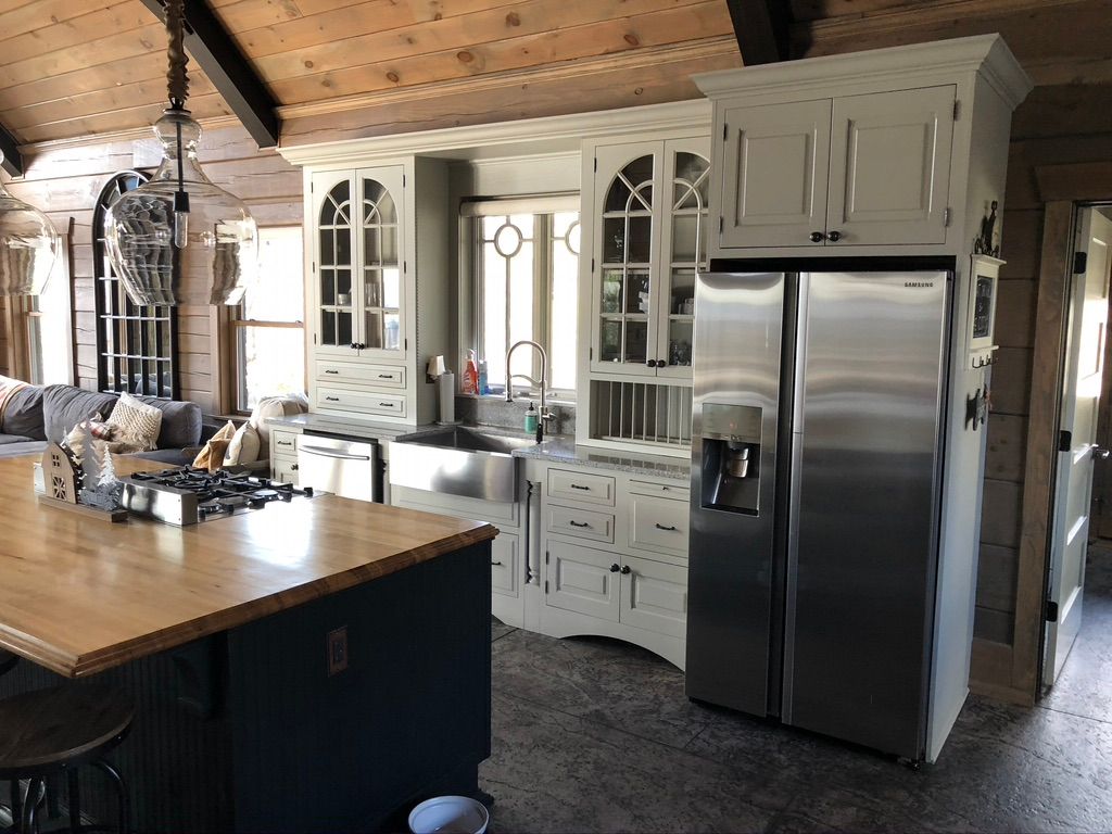 Before the Remodeling: A rustic kitchen with a vaulted wooden ceiling, stainless steel refrigerator, and farmhouse sink showcases a stunning before/after transformation with white cabinetry, a wooden island, and abundant natural light for a warm, cozy atmosphere.