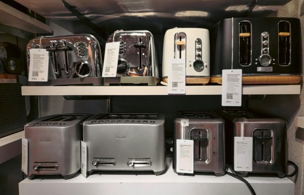 A store display showcases the appliance selection in Weehawken, with two shelves of modern toasters. The top shelf features four chrome, white, and black toasters, while the bottom shelf displays three metallic models, each tagged with product information.